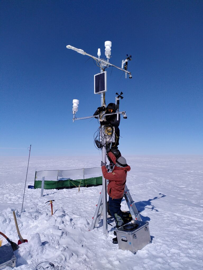 On the ice sheet, two persons building a weather station.