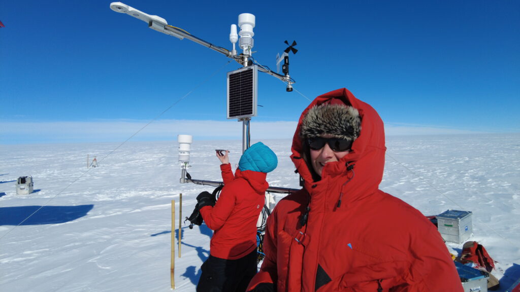 Two persons on the ice sheet in read clothing. Weather station in the background.