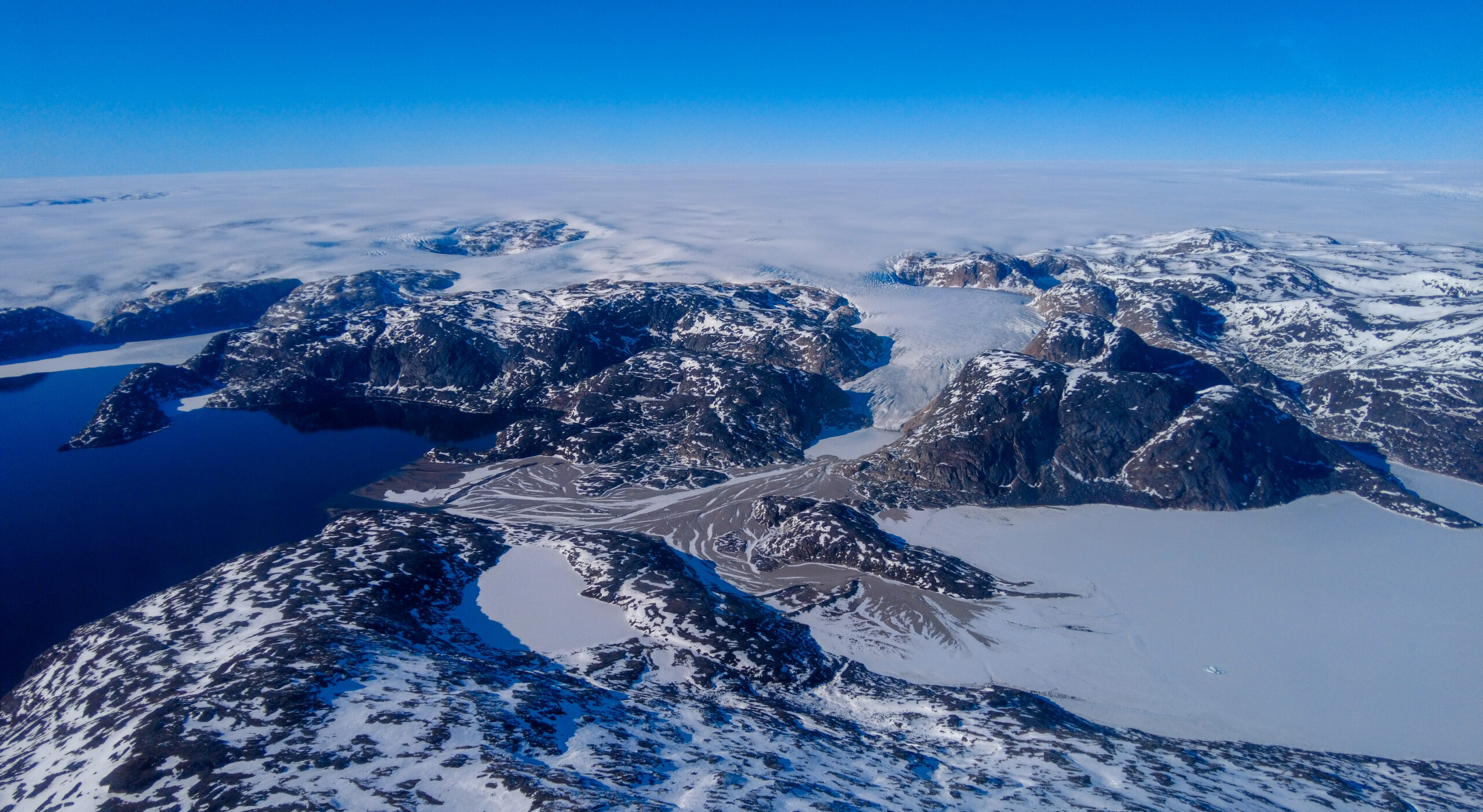 View of South Greenland glacier from the air. Blue skies and mountaineous landscape.